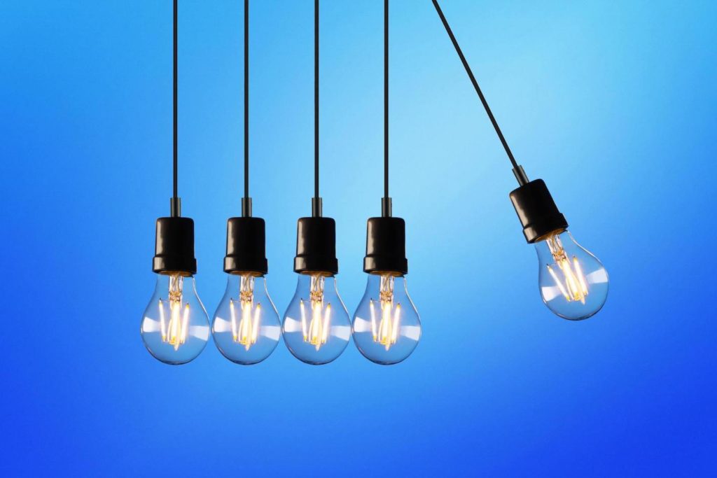 Blue background with 5 dangling light bulbs in wires one is about to hit the others like an office desk toy